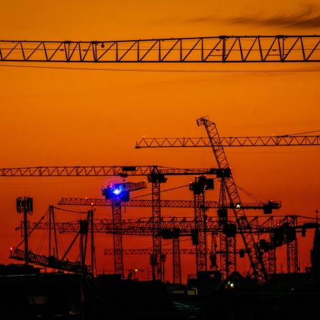Viele Baukräne sind nach Sonnenuntergang vor dem Abendhimmel zu sehen.