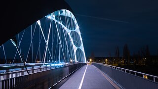 Blick auf eine beleuchtete Frankfurter Brücke in der Nacht. Logo: Buchmesse 2021