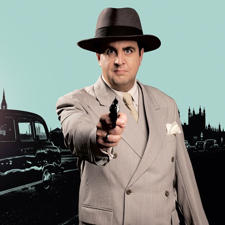 Bastian Pastewka steht in Anzug vor der Kulisse Londons und zielt mit einer Pistole.