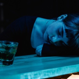 Eine Frau ist am Tisch eingeschlafen, während sie noch ein Glas mit einem Drink festhält.