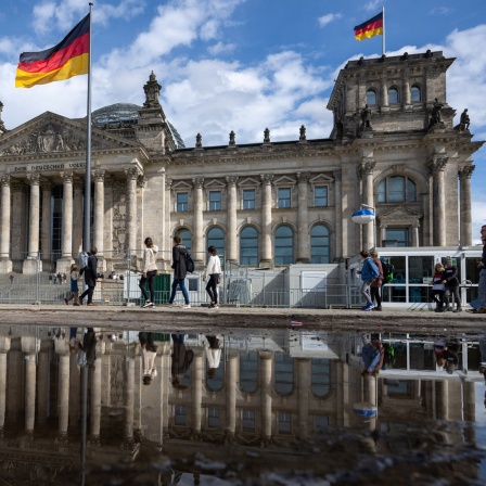 Passanten gehen beim sonnigen Wetter an dem Reichstagsgebäude vorbei. 