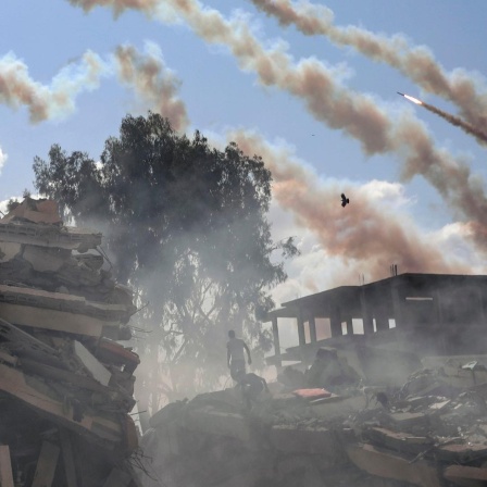 Palästinensische Gebiete, Gaza-Stadt: Raketen aus dem Gazastreifen werden über zerstörte Gebäude hinweg auf Israel abgefeuert.