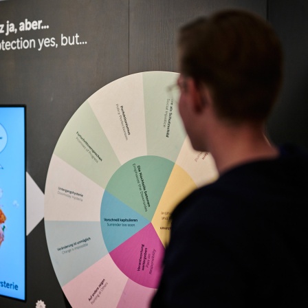 Ein Mann steht vor einer Wand mit der Aufschrift "Klimaschutz ja, aber" in der Ausstellung "Klima_X".