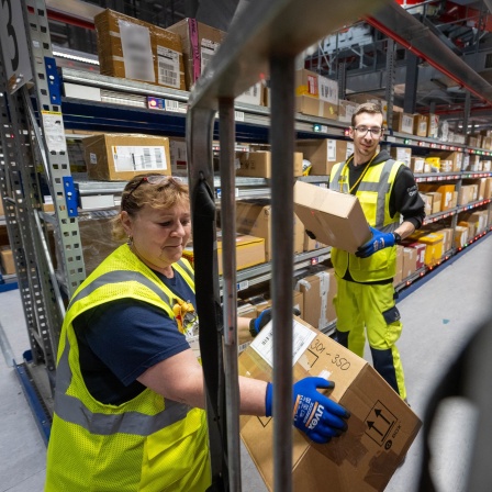 Mitarbeiter am DHL Hub in Leipzig sortieren Pakete für die Überprüfung durch den Zoll auf einen Wagen.