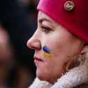 Profil einer Demonstrantin mit einer roten Mütze und einer gemalten ukrainischen Flagge auf der Wange.