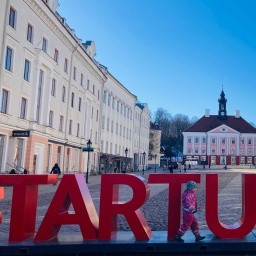 Ein mit weißen Fähnchen geschmückter Marktplatz auf dem ein roter Schriftzug steht "Tartu 2024".