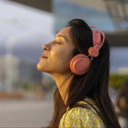Eine junge Frau mit Kopfhörern und geschlossenen Augen scheint in entspannter Stimmung zu sein