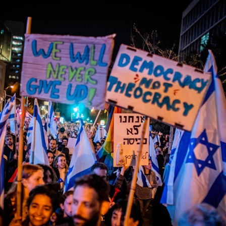 Demonstranten halten am 25. März 2023 in Tel Aviv / Israel Fahnen und Plakate in die Höhe. Auf einem steht &#034;Democracy not Theocracy&#034;. Der Protest richtet sich gegen Pläne der Regierung, das Justizsystem umzustrukturieren.