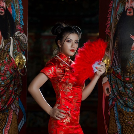 Eine stark gestylte Frau in traditionellem chinesischen roten Kleid und rotem Fächer.