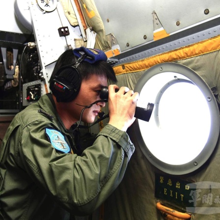 Ein Mann schaut mit einem Fernglas durch ein Flugzeugfenster nach draußen.