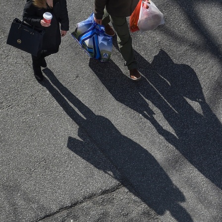 Zwei Personen mit langen Schatten, der auf eine Straße fällt, tragen ihren Einkauf.
