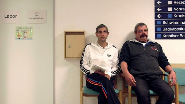 Michel Abdollahi (l.) sitzt mit einem Mann vor einer Tür in einer Rehaklinik.