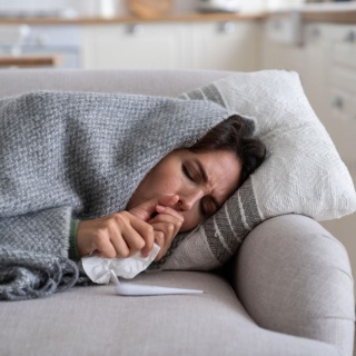 Eine Frau liegt unter einer Decke hustend auf dem Sofa. (Bild: picture alliance/Zoonar/Dmitrii Marchenko) 