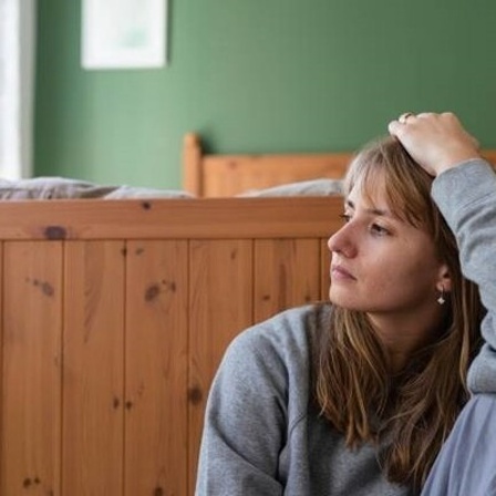 Eine junge Frau sitzt nachdenklich auf dem Boden vor einem Bett