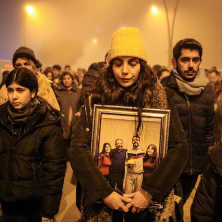 Eine Gruppe von Menschen erinnert in der türkischen Provinz Hatay den Opfern des Erdbebens vom Februar 2023. Eine Frau hält ein Foto in den Händen, das eine Familie zeigt. Die Frau hat die Augen geschlossen. (5.2.2024)