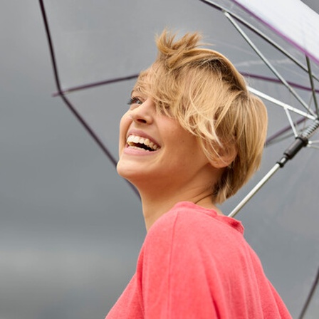 Eine lächelnde junge Frau unter einem Regenschirm. Dunkle Wolken am Himmel.
