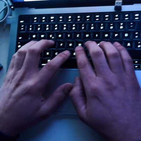 Ein Mensch tippt im Dunkeln etwas auf einr PC-Tastatur.