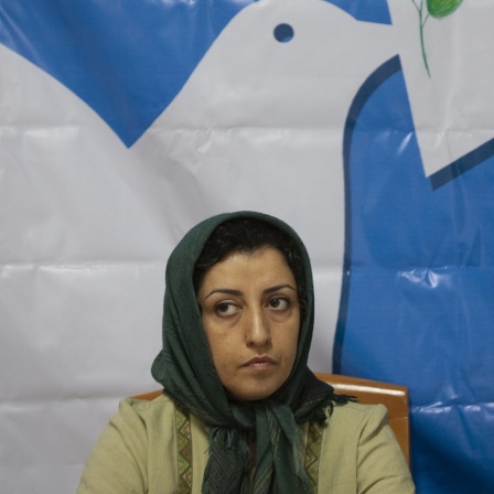 Eine Frau mit Kopftuch sitzt vor einem Plakat mir einer Friedenstaube.