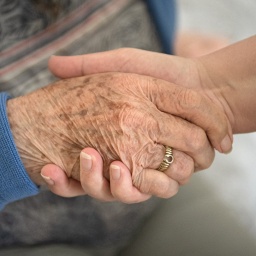 Eine Pflegefachkraft hält die Hand einer Pflegeheim-Bewohnerin 