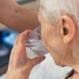 Eine ältere Frau trinkt aus einem Glas Wasser. Hitze kann lebensgefährlich sein - das weisen auch offizielle Statistiken nach