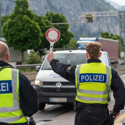 Ein Polizist stoppt an der deutsch-österreichischen Grenze ein Fahrzeug auf der Autobahn mit einer Polizeikelle mit Aufschrift: HALT POLIZEI.