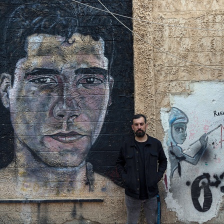 Der Palästinenser Ahmed Tobasi, der künstlerische Leiter des Freedom Theatre, das von Zakaria Zubeidi, einem Anführer der al-Aqsa-Märtyrerbrigaden im Westjordanland, mitbegründet wurde, posiert für ein Foto vor Graffiti, das Zubeidi im Freedom darstellt.