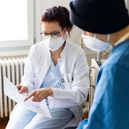 Personen mit Mund- Nasenschutz in einem Krankenzimmer