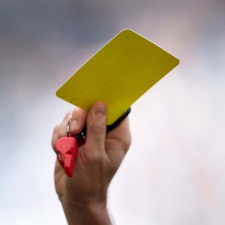 Symbolbild: Schiedsrichter:in hält eine gelbe Karte und eine Pfeife in der erhobenen Hand