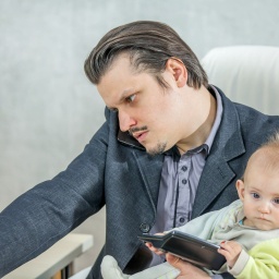 Ein junger Geschäftsmann arbeitet in seinem Büro und hält ein Baby