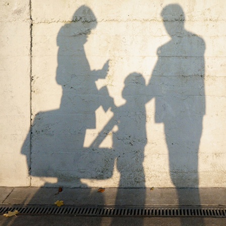 Die Schatten einer Frau, eines Kindes und eines Mann vor einer Mauer.