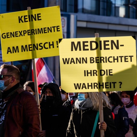 Die Teilnehmer einer Demonstration gegen die Corona-Maßnahmen gehen den Friedrichring entlang und halten Schilder mit den Aufschriften "Keine Genexperimente am Mensch!" und "Medien - wann berichtet ihr die Wahrheit?" in der Hand.