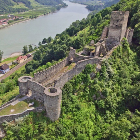 Die Donau aus Vogelflugperspektive, am Ufer windet sich eine große lange Burg auf einem Hügel