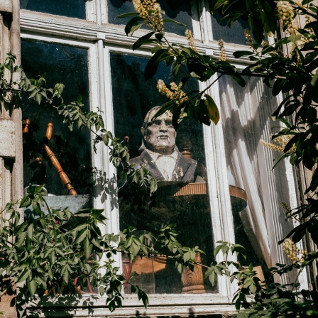 Graf-Dracula-Statue blickt aus dem verschlossenen Fenster eines alten Gebäudes.