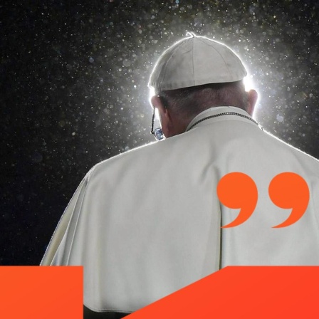 Papst Franziskus ist von hinten zu sehen, er sitzt vor einem Mikrofon. Von vorne wird er von einem Lichtkegel angestrahlt. 