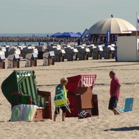 Zwei Personen stehen neben Strandkörben an einem Strand.