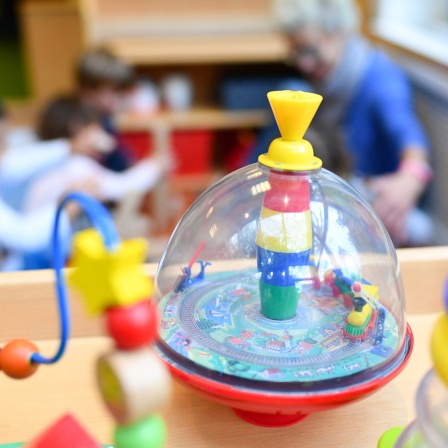 Spielzeug steht im Vordergrund, dahinter sind spielende Kinder zu sehen.