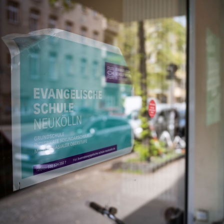 An der Schulfassade hängt eine Plakat mit der Aufschrift Evangelische Schule Neukölln; © picture alliance/dpa/Hannes P Albert