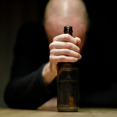 Ein Mann sitzt an einem Tisch und hält eine Flasche Bier in der Hand.