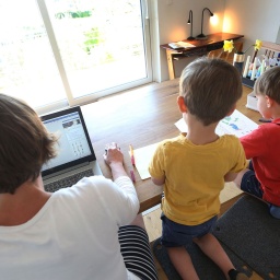 Corona-Krise – Die Mutter des sechsjährigen Jakob und des vierjährigen Valentin arbeitet Zuhause an einem Laptop, während ihre Kinder neben ihr malen und ein Buch ansehen. © picture alliance/dpa | Karl-Josef Hildenbrand 
