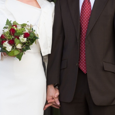 Ein Hochzeitspaar steht am nach der Trauung vor dem Standesamt.
