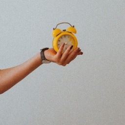 Eine Frauenhand, die einen gelben Wecker in der linken Hand hält