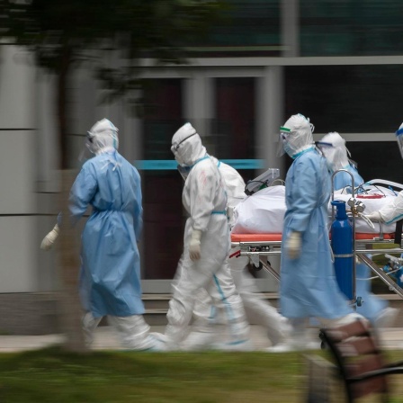 Menschen in Schutzkleidung transportieren einen Patienten. 