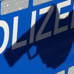 Schatten einer Waffe auf dem Schriftzug "POLIZEI" an der Tür eines Einsatzfahrzeugs. Symbolbild