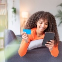 Smiling woman holding credit card using mobile phone at home model released
