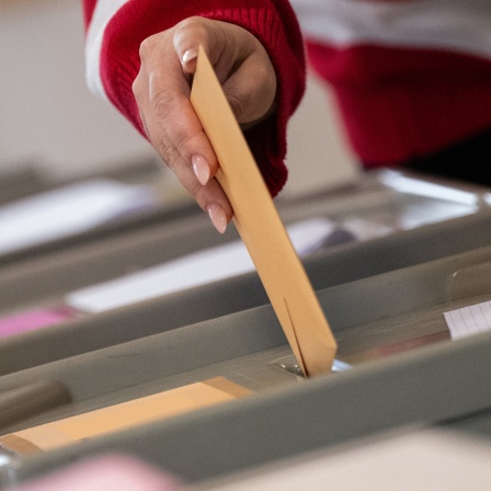 Eine Hand wirft einen Wahlzettel in eine Wahlurne