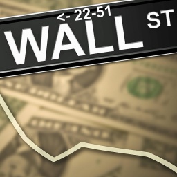 Auf einer Grafik von Dollarscheinen und dem Schild Wallstreet verläuft eine abfallende Börsenkurve.