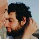 Eine Frau mit Hijab, die einen Mann zärtlich umarmt und mit der Nase an der Stirn berührt.