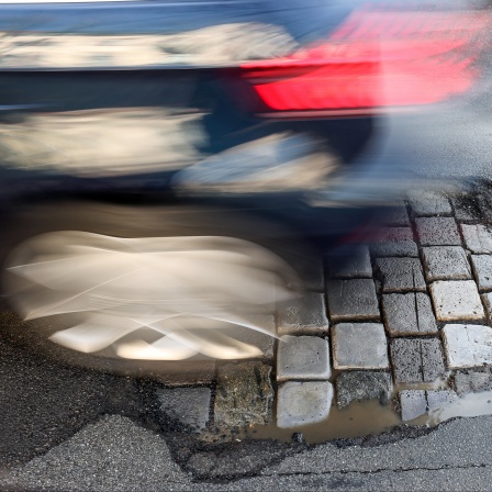 Ein Auto fährt über eine Straße mit Schlaglöchern. 