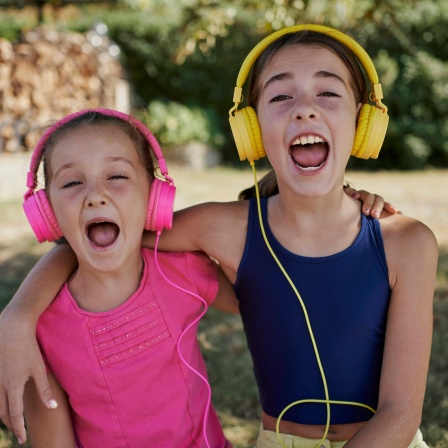 Zwei Mädchen mit Kopfhörern singen mit weit geöffneten Mündern