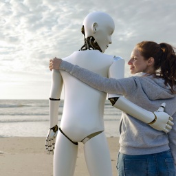 Ein Roboter und ein Frau stehen Arm in Arm am Strand